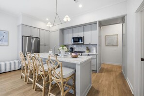A modern kitchen with grey cabinets, a stainless steel refrigerator, a microwave, and a dining area with wicker chairs.