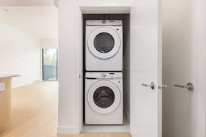 Une buanderie équipée d’un lave-linge et d’un sèche-linge Samsung, avec un plancher en bois et une vue par la porte.