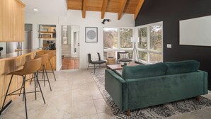 Eine moderne Küche mit Holzausstattung, ein Essbereich mit einem grünen Sofa und Blick durch große Fenster.