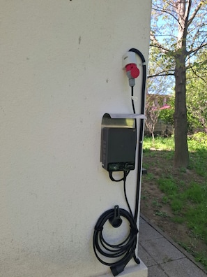 Estação de carregamento elétrica externa fixada em parede, com cabo conectado.