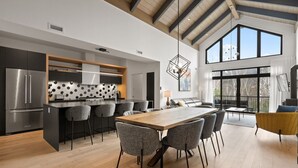 Una cocina moderna con una isla central, una zona de comedor con una mesa grande y un espacio de sala de estar con un sofá y televisión.