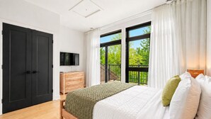 Un dormitorio con cama, televisor, cómoda y balcón con vistas.