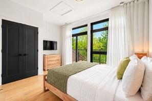 Een slaapkamer met een bed, een televisie, een kaptafel en een balkon met uitzicht.