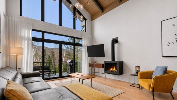 Una sala de estar moderna con chimenea, un sofá, un sillón amarillo y un televisor montado en la pared.