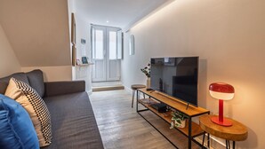 A modern living room with a sofa, TV, and a small table with a lamp. - The Bica Secret Nest by LovelyStay (Lisboa)