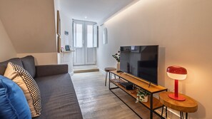 Ein modernes Wohnzimmer mit einer Couch, einem Fernseher und einem kleinen Tisch mit einer Lampe.