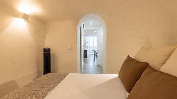 A bedroom with a bed, pillows, a radiator, and an arched doorway leading to a hallway. - The Bica Secret Nest by LovelyStay (Lisboa)