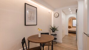 A dining area with a round wooden table, a framed picture, a potted plant, and a clock on the wall. - The Bica Secret Nest by LovelyStay (Lisboa)
