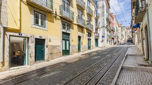 A narrow street with buildings on either side, a tram track, and a visible hotel entrance with a green door. - The Bica Secret Nest by LovelyStay (Lisboa)