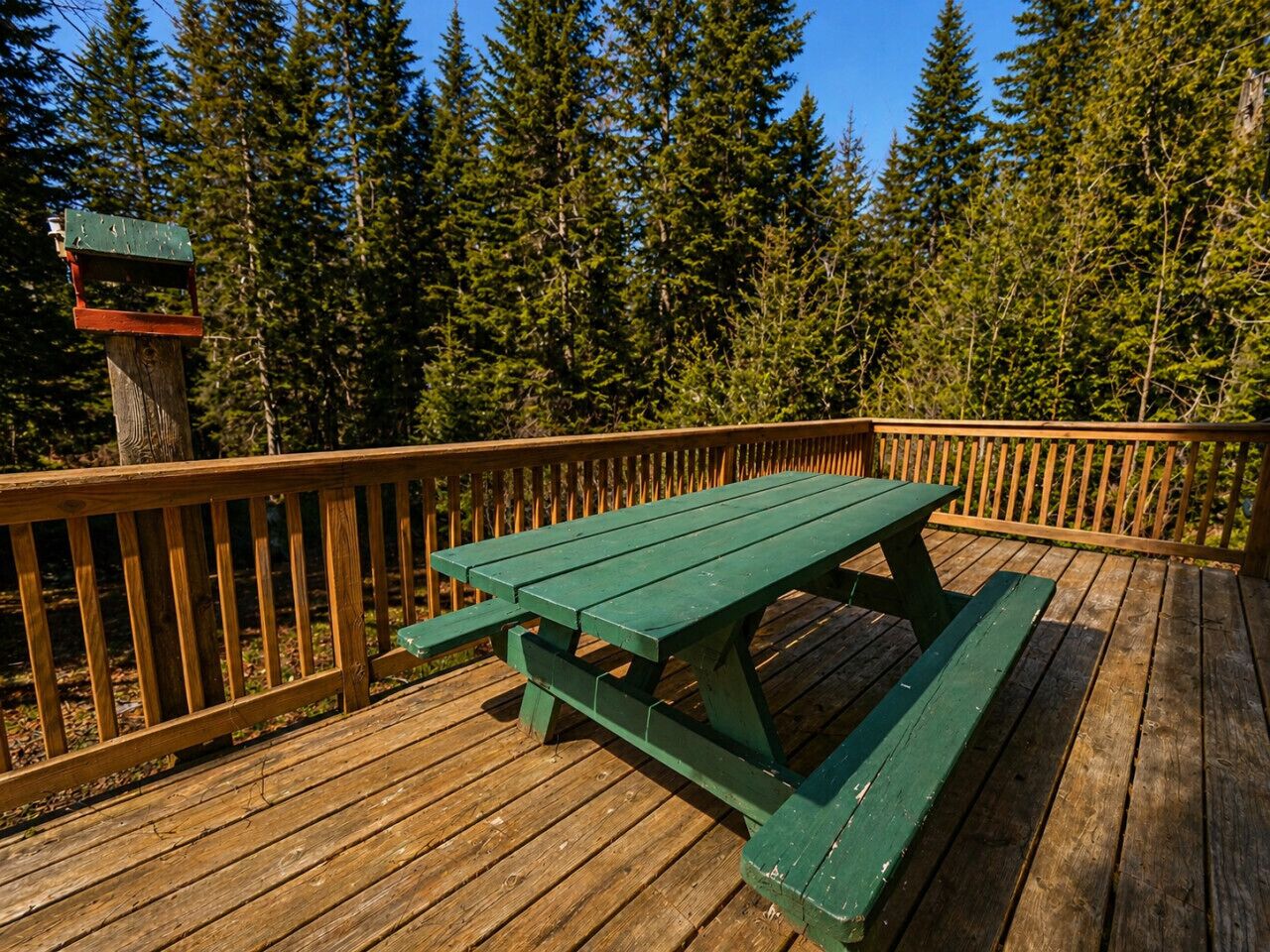 A wooden deck with a picnic table and a birdhouse.