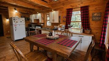 A wooden cabin interior with a dining table, chairs, a refrigerator, and a kitchen area.