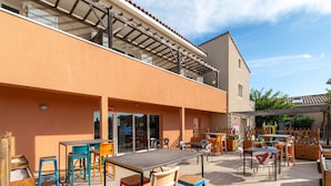 An outdoor patio area with tables and chairs, a covered seating area, and a building with a tiled roof.