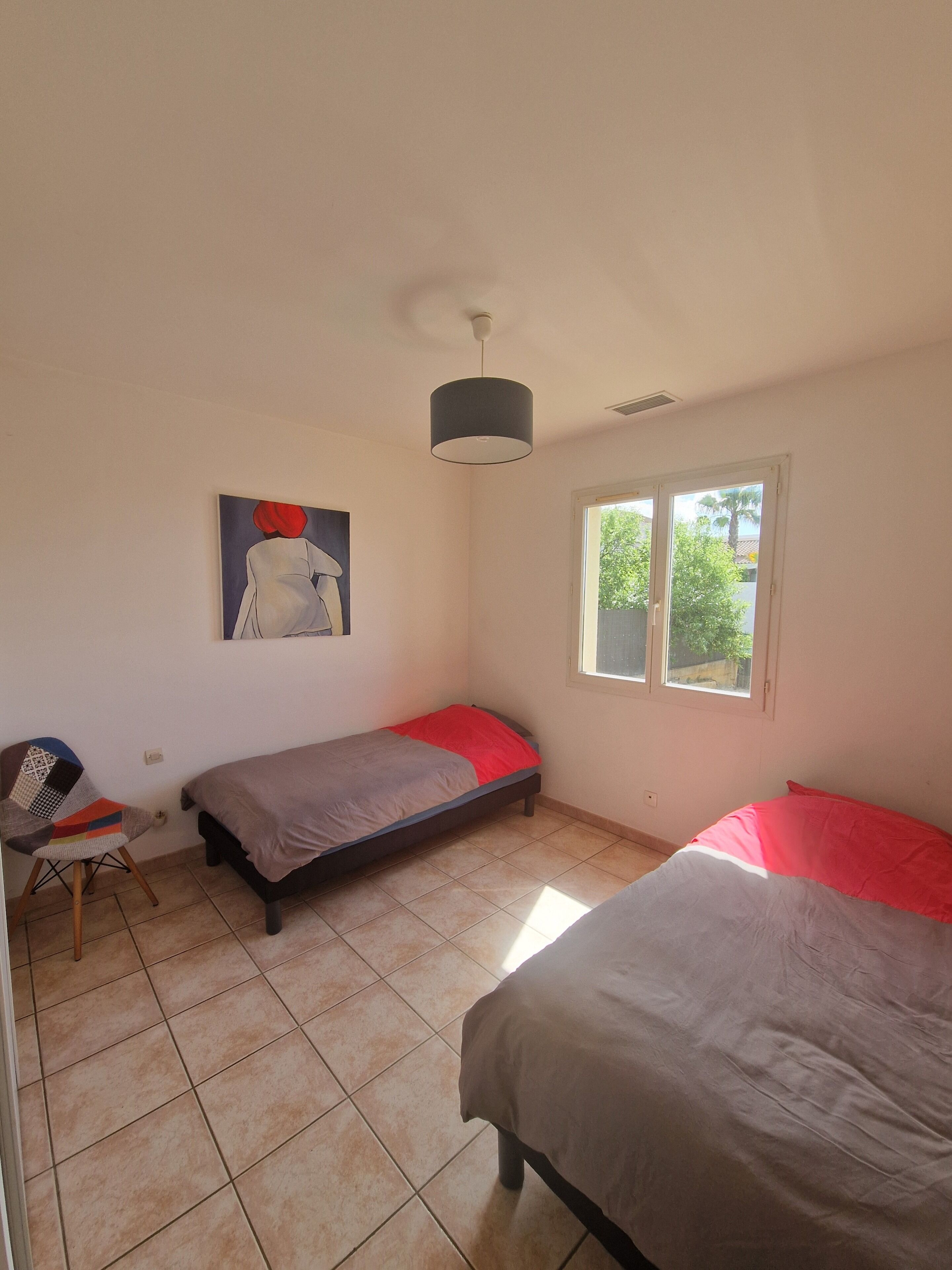 A bedroom with two single beds, a chair, a painting, and a window.