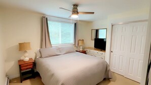 A bedroom with a bed, nightstands, a ceiling fan, a dresser, a mirror, and a door. - MBA- New Apt w/Direct Access Snowmobile/ATV Trail (Presque Isle)