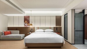 A modern hotel room with a large bed, a sofa, a bedside table, and a wardrobe.