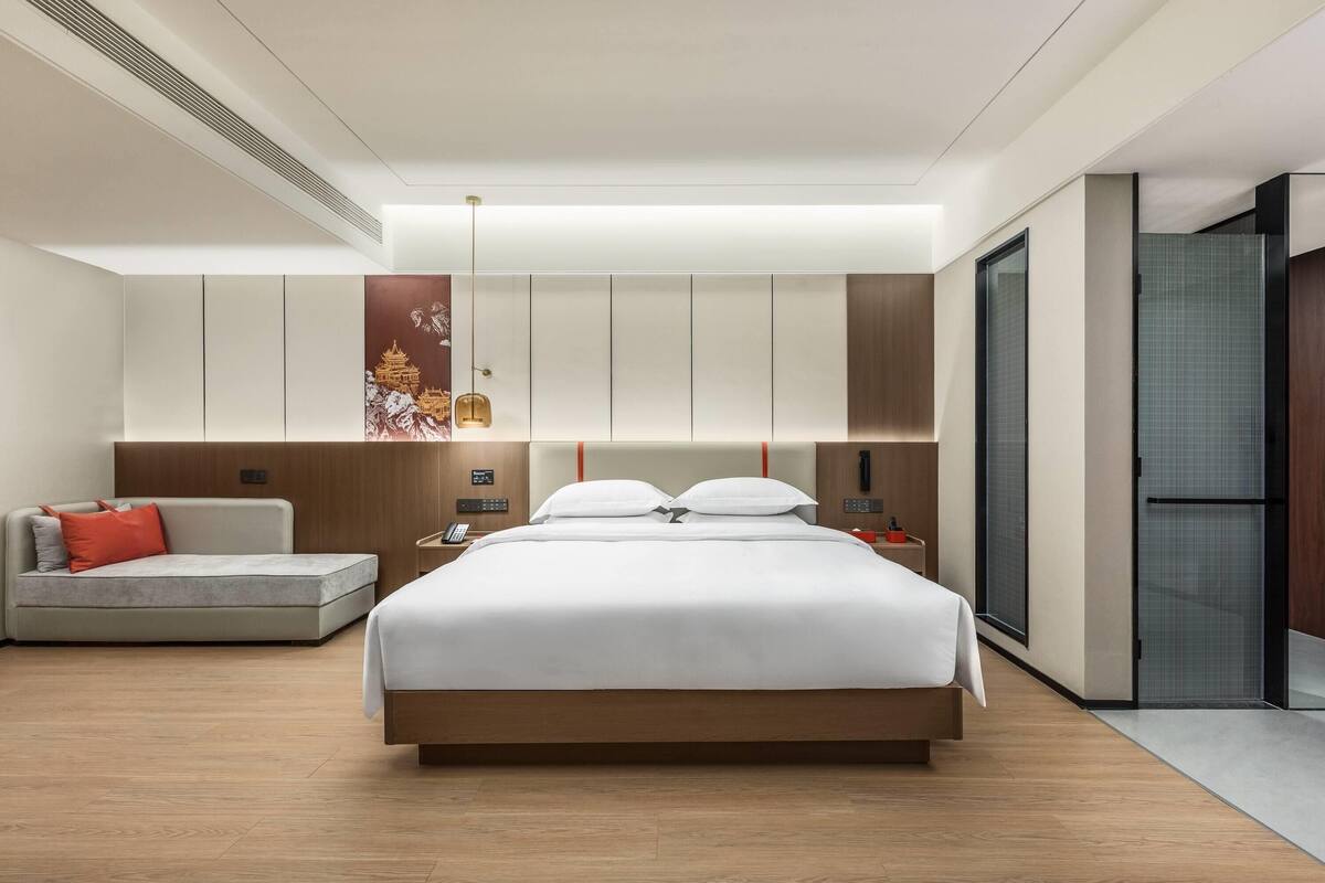 Una habitación de hotel moderna con una cama grande, un sofá, una mesita de noche y un armario.