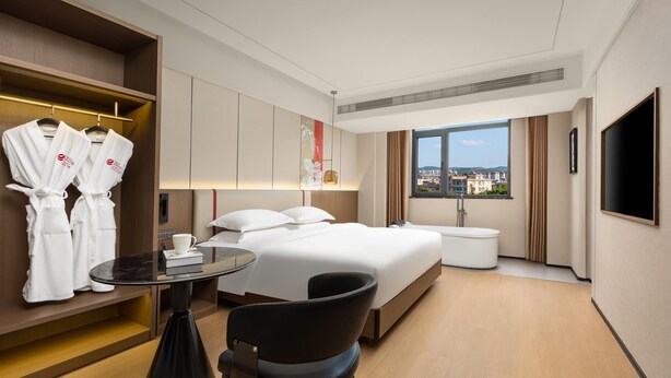A hotel room with a bed, a desk, a chair, a TV, and a window with a city view.