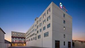 A modern hotel building with a flat facade, multiple windows, and a prominent logo on the top.