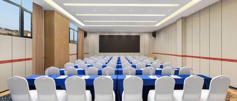 A conference room with rows of tables, white chairs, and a large screen.