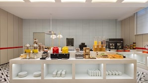 A buffet setup with various food items and utensils, a mirror, and a tiled wall.