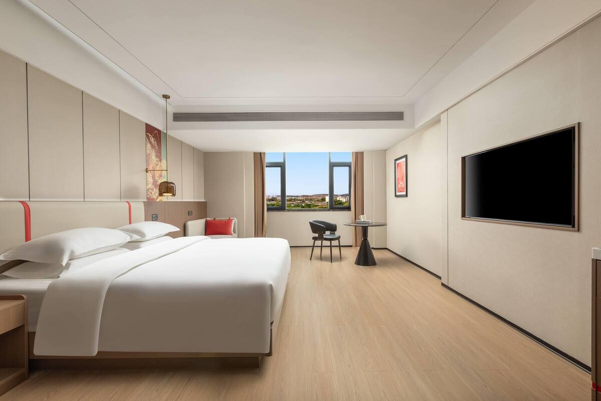 Habitación de hotel con cama, televisor, escritorio y ventana con vistas.