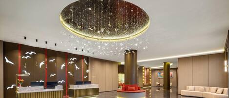 A modern lobby with a reception desk, a large circular chandelier, and a plush sofa.