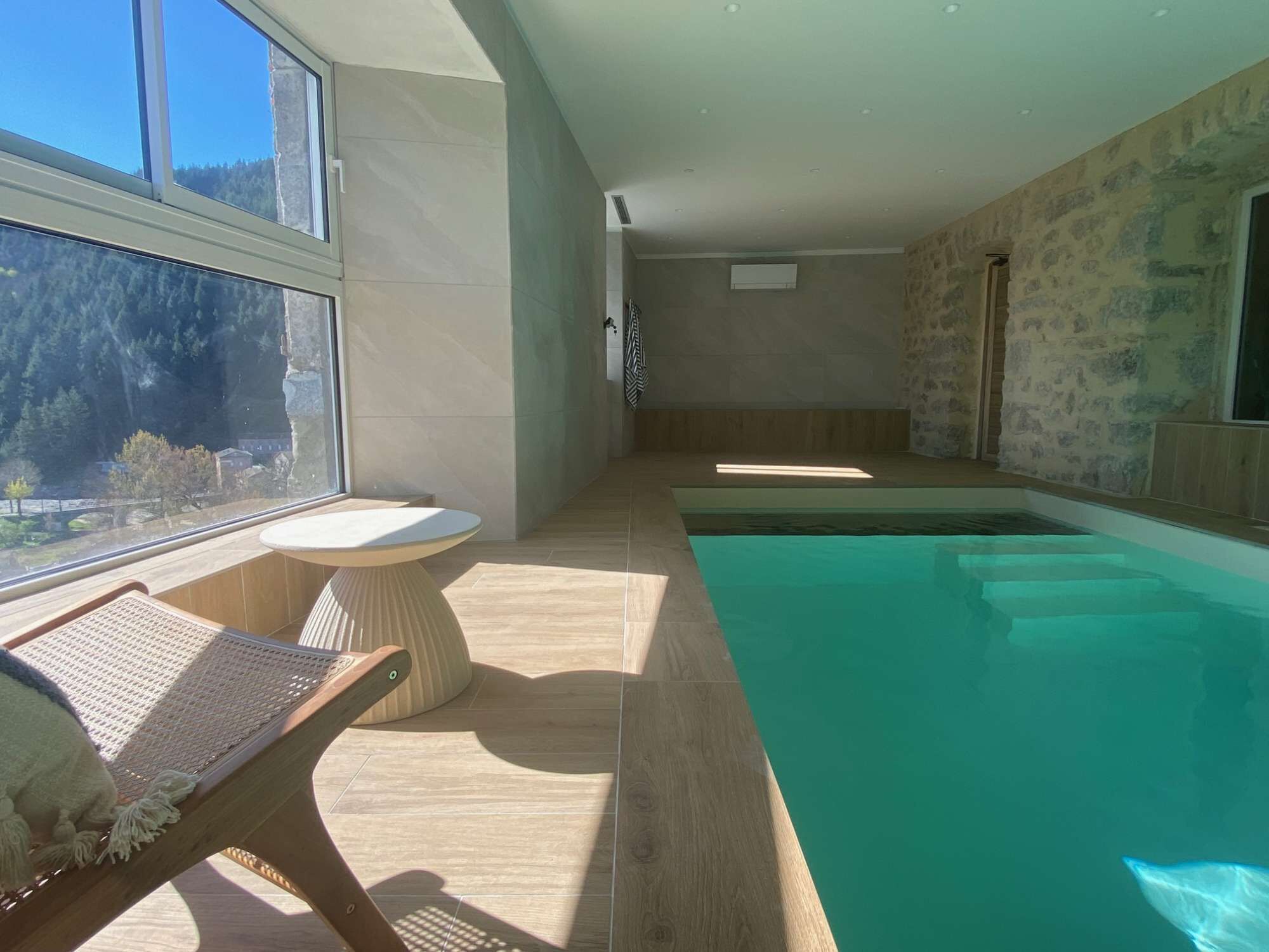A modern indoor swimming pool with a view of a forested area through large windows.