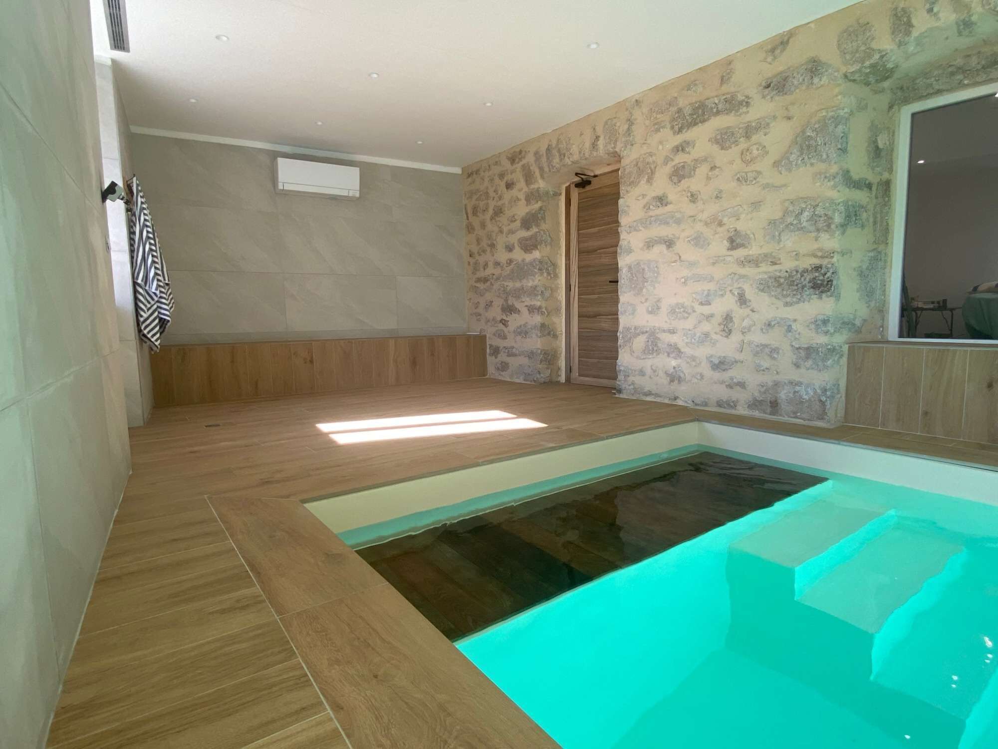 Une salle de bain moderne avec un jacuzzi entouré de parois en verre, un plancher en bois et des murs en pierre.