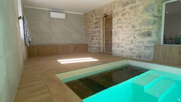 Une salle de bain moderne avec un jacuzzi entouré de parois en verre, un plancher en bois et des murs en pierre.