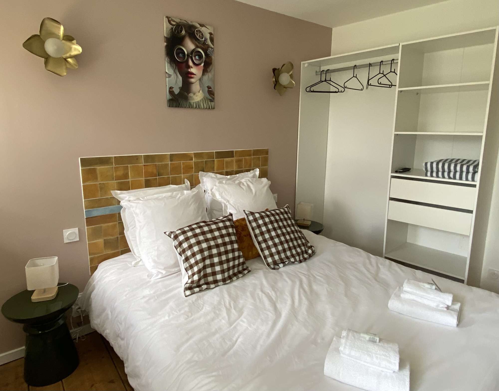 Ein Hotelzimmer mit Bett, Kissen, Nachttisch, Lampe, Wandbild, Kleiderschrank und Spiegel.
