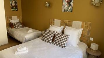 Une chambre d’hôtel avec deux lits, chacun étant équipé de draps blancs et d’oreillers à carreaux. Il y a des serviettes sur les lits et une petite table de chevet avec une lampe.