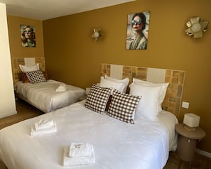 Habitación de hotel con dos camas, cada una con ropa blanca y almohadas a cuadros. Hay toallas sobre las camas y una mesita de noche con una lámpara.