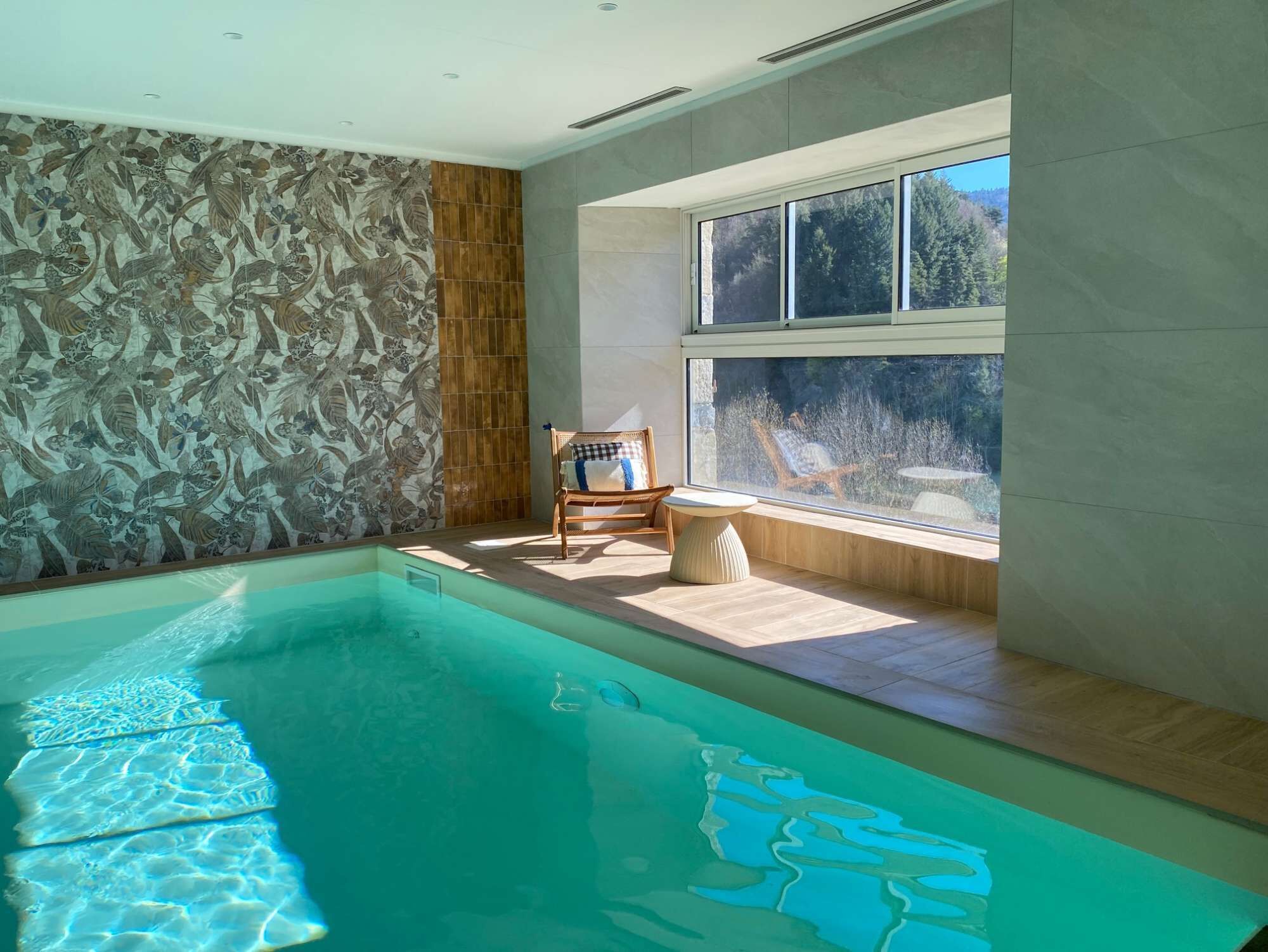 A modern indoor swimming pool with a clear view of the outdoors through a large window.