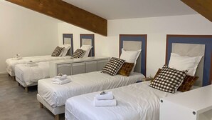 A hotel room with four single beds, each with a pillow and a folded towel.