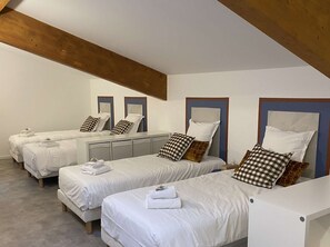 A hotel room with four single beds, each with a pillow and a folded towel.