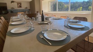 A dining table set with plates, glasses, and cutlery, with a view of a forest through a large window.