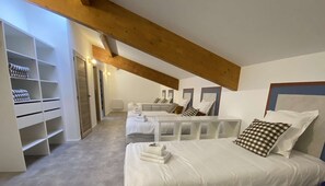 Quarto com teto inclinado, cama com roupa de cama branca, guarda-roupa e espelho.
