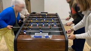 A group of people playing foosball in a room with wooden flooring and a door in the background.