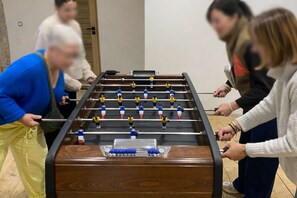 A group of people playing foosball in a room with wooden flooring and a door in the background.