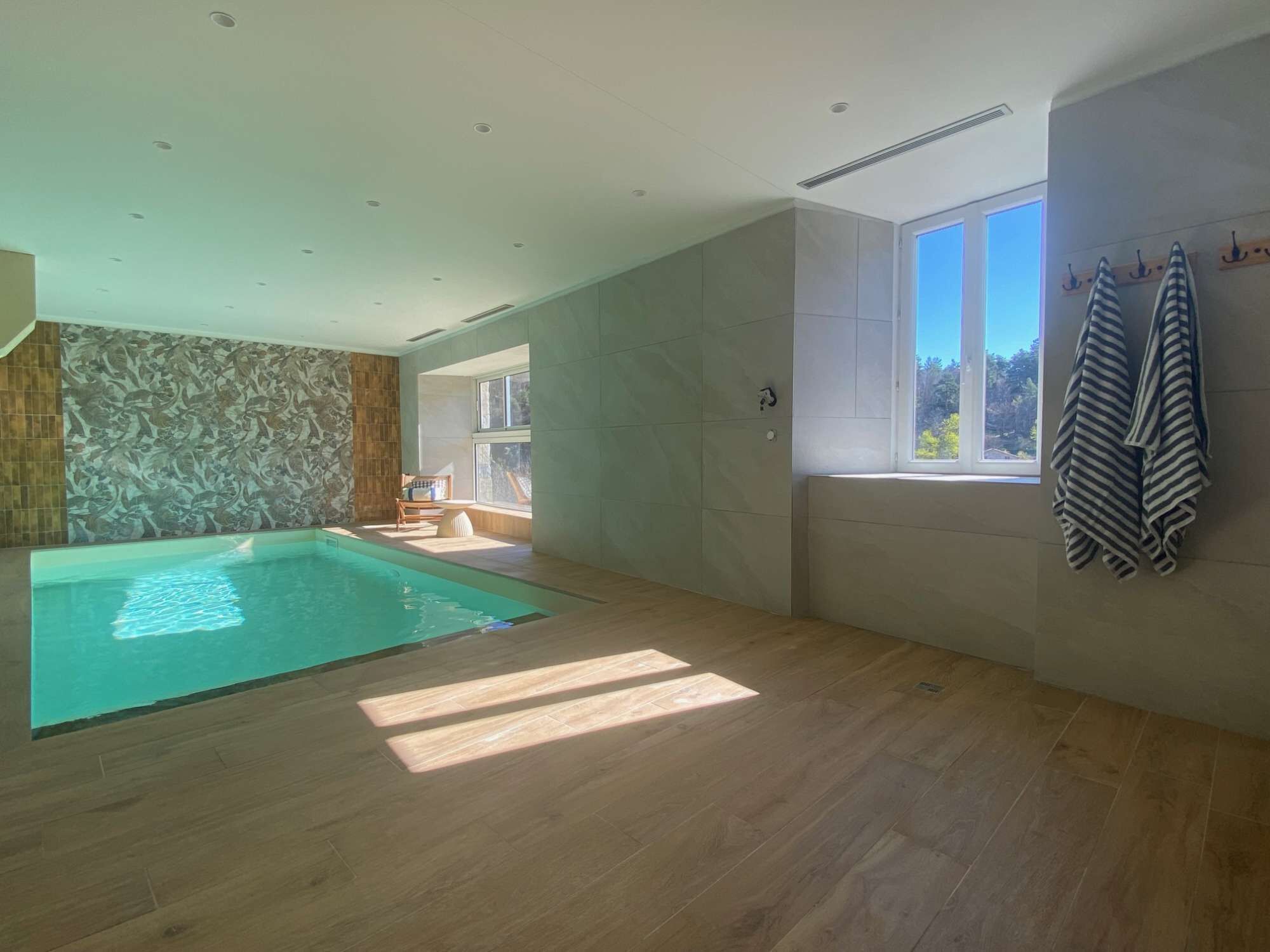 Un vaste espace abritant une piscine intérieure, avec une vue sur l’extérieur grâce à une grande baie vitrée.