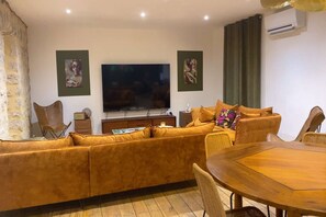 Uma sala de estar com sofá, televisão, mesa de jantar e uma cadeira.