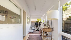 A narrow hallway with a wooden floor, a patterned rug, a grey armchair, a small table with a lamp, and a bookshelf. - Woodstock Waterfall Hideaway · Walk To Tinker St! (Woodstock)