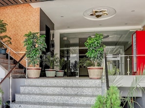 A modern building entrance with a stone wall, a glass door, and a red door.