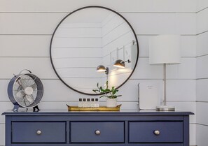 A vanity with a round mirror, two wall-mounted lamps, a fan, and a potted plant.