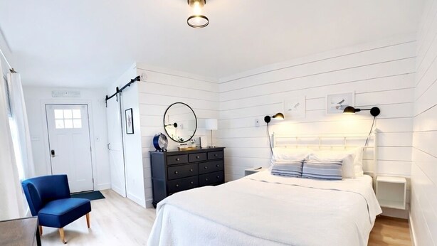 A bedroom with a bed, bedside tables, a dresser, a chair, a mirror, and a ceiling light fixture. - Downtown Ogunquit!  Steps to the Beach, Dining & Shops! Park & Walk Everywhere! (Ogunquit)