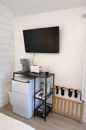 Una kitchenette equipada con refrigerador, tostadora, cafetera y televisor instalado en la pared.