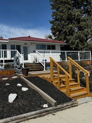 A house with a red roof, white exterior, and a wooden deck with a staircase leading to a porch. - Convenient Location Near Large Shopping Mall and Train Station. (Calgary)