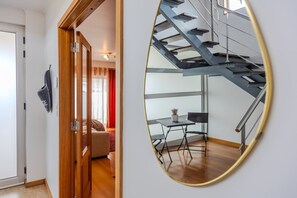 A modern interior with a wooden door, a mirror reflecting a staircase, and a dining area with a table and chairs. - GuestReady - Casa Santa Maria (Ponta Delgada)