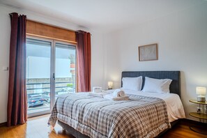Een hotelkamer met een bed, nachtkastje, lamp, raam met gordijnen en uitzicht.