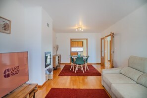 A modern living room with a sofa, a dining area with a table and chairs, a TV, and a kitchen visible through an open door. - GuestReady - Casa Santa Maria (Ponta Delgada)